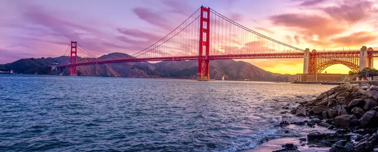 A Ponte Golden Gate ao pôr do sol com um céu multicolorido e a Baía de 贝博体彩app em primeiro plano.